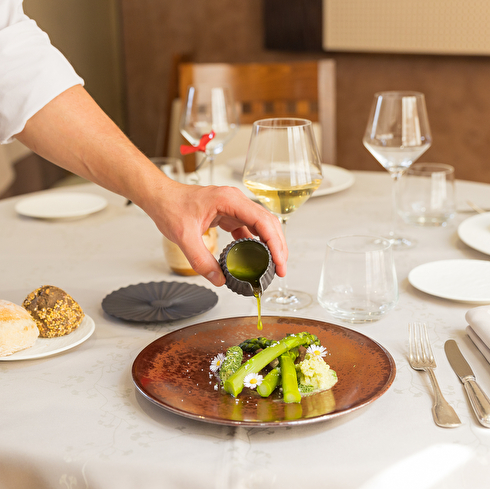 Table dressée avec une assiette d'asperges sur laquelle le chef verse une sauce.